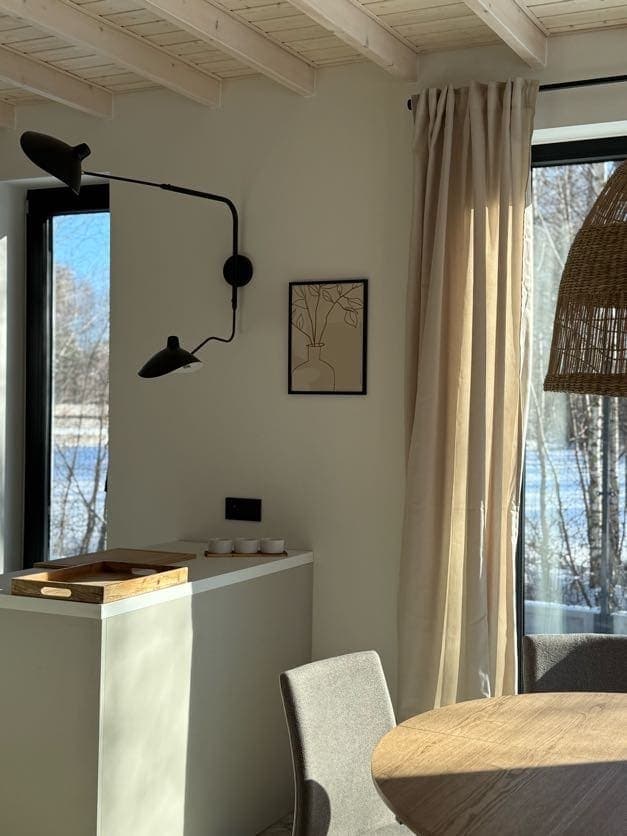 Aneks kuchenny z designerskim kinkietem, obrazem i zasłonami przy panoramicznym oknie na las